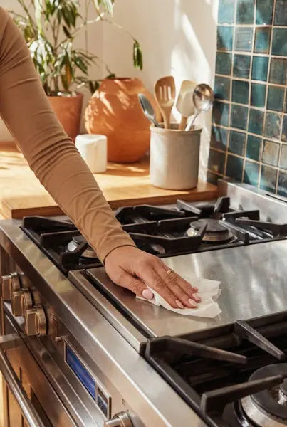 woman cleaning stove with vinegar wipe